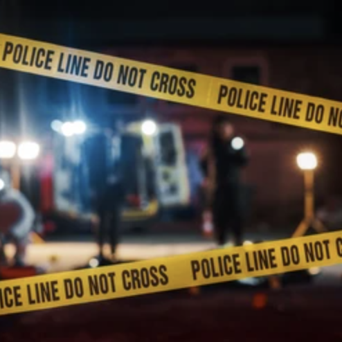 Yellow police tape reading Police Line Do Not Cross in front of a blurred crime scene at night